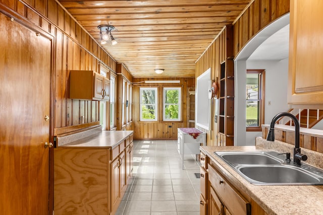 kitchen featuring a sink, wood ceiling, wood walls, light countertops, and arched walkways