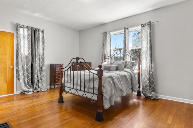bedroom featuring a textured ceiling, visible vents, baseboards, and wood-type flooring