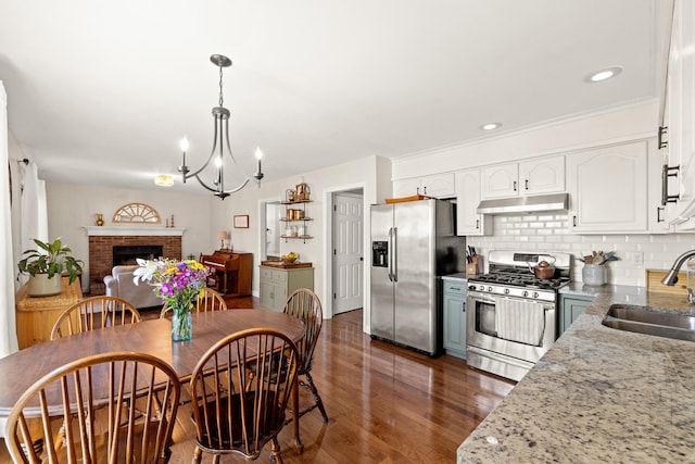 kitchen with dark wood-style flooring, a sink, a chandelier, stainless steel appliances, and under cabinet range hood