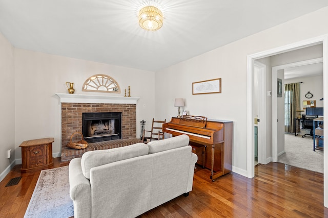 living area featuring visible vents, baseboards, a brick fireplace, and wood finished floors