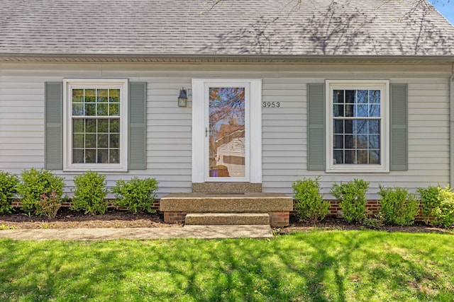 property entrance with roof with shingles and a lawn