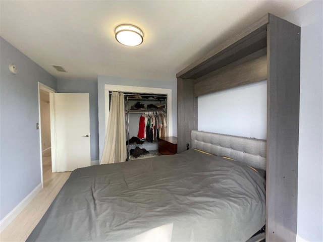 bedroom featuring wood finished floors, baseboards, visible vents, and a closet
