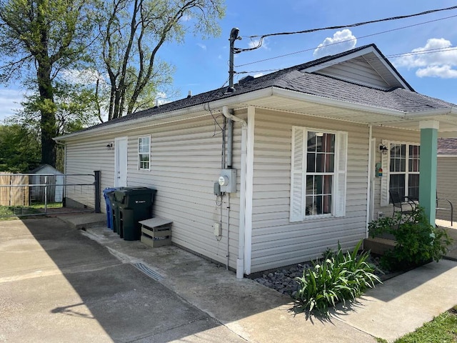 view of side of property with a shingled roof, covered porch, and fence