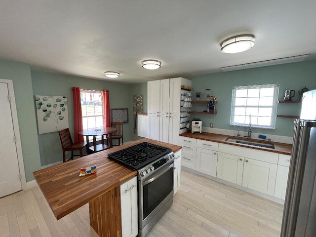 kitchen featuring butcher block countertops, stainless steel appliances, open shelves, white cabinets, and a sink