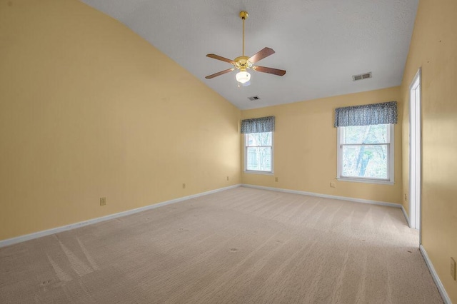 empty room with visible vents, vaulted ceiling, light colored carpet, and baseboards