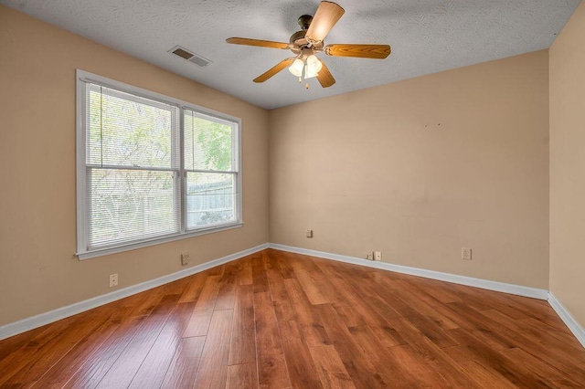 spare room featuring wood finished floors, visible vents, ceiling fan, and baseboards