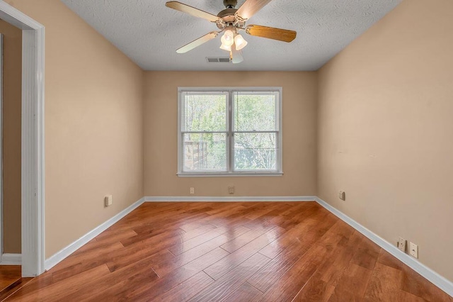 empty room featuring a ceiling fan, visible vents, baseboards, a textured ceiling, and wood finished floors