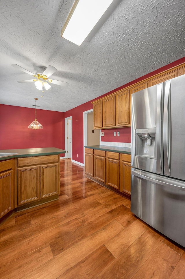 kitchen with light wood-style floors, stainless steel fridge, ceiling fan, brown cabinetry, and a textured ceiling
