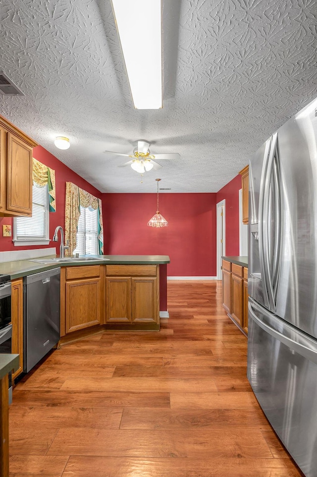 kitchen featuring a sink, appliances with stainless steel finishes, visible vents, a peninsula, and brown cabinetry