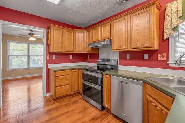 kitchen featuring light wood-style flooring, brown cabinetry, stainless steel appliances, under cabinet range hood, and ceiling fan