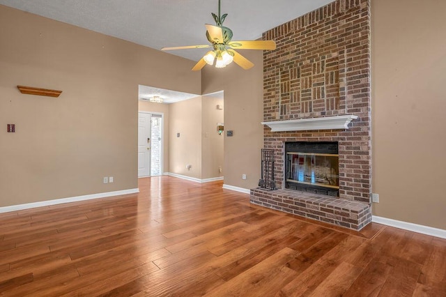 unfurnished living room with a brick fireplace, hardwood / wood-style flooring, a ceiling fan, and baseboards
