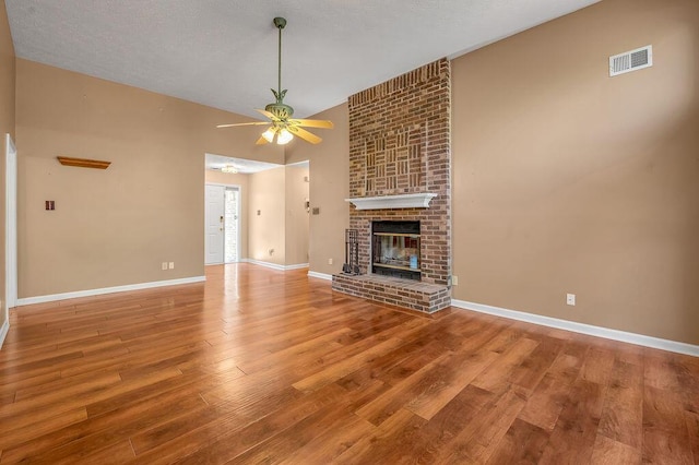 unfurnished living room with wood finished floors, ceiling fan, a fireplace, baseboards, and visible vents