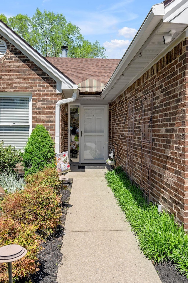 view of exterior entry featuring brick siding and roof with shingles