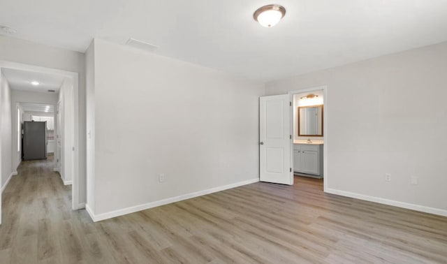 unfurnished bedroom with light wood-type flooring, ensuite bath, freestanding refrigerator, and baseboards