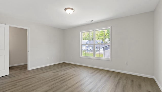 spare room featuring wood finished floors, visible vents, and baseboards