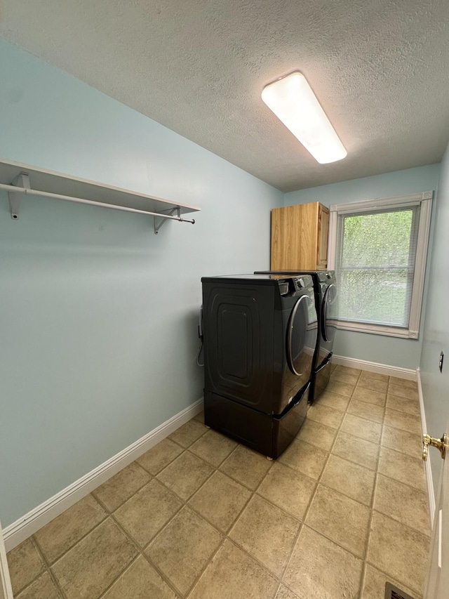laundry room featuring a textured ceiling, light tile patterned floors, washing machine and dryer, baseboards, and cabinet space