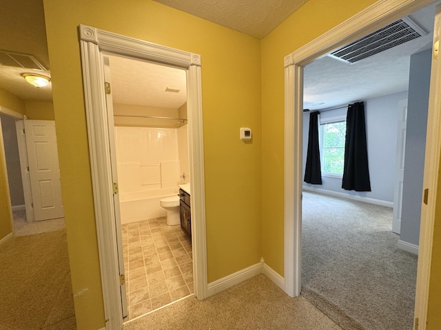 hallway with light colored carpet, visible vents, a textured ceiling, and baseboards