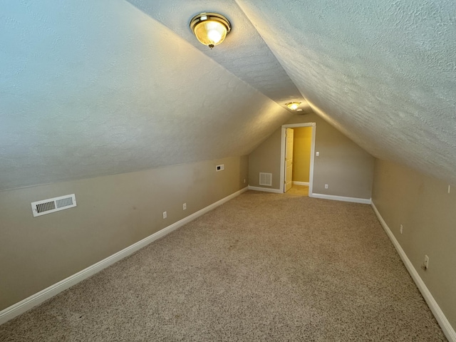 additional living space featuring a textured ceiling, visible vents, and vaulted ceiling