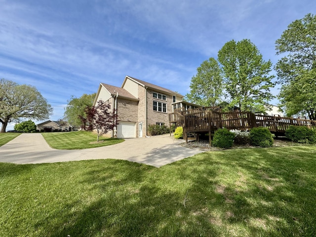 back of property with an attached garage, brick siding, a wooden deck, concrete driveway, and a lawn
