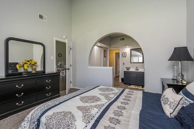 carpeted bedroom with a high ceiling, a sink, arched walkways, and visible vents