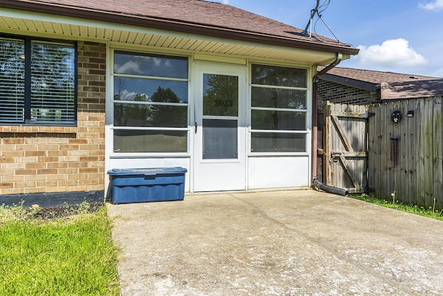 exterior space featuring a gate, a patio area, roof with shingles, fence, and brick siding