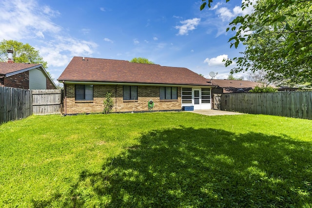 rear view of house with a patio, roof with shingles, a lawn, brick siding, and a fenced backyard