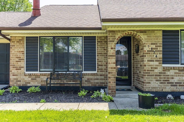 property entrance featuring brick siding and a shingled roof
