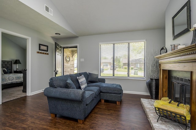 living room featuring lofted ceiling, visible vents, baseboards, a glass covered fireplace, and wood finished floors