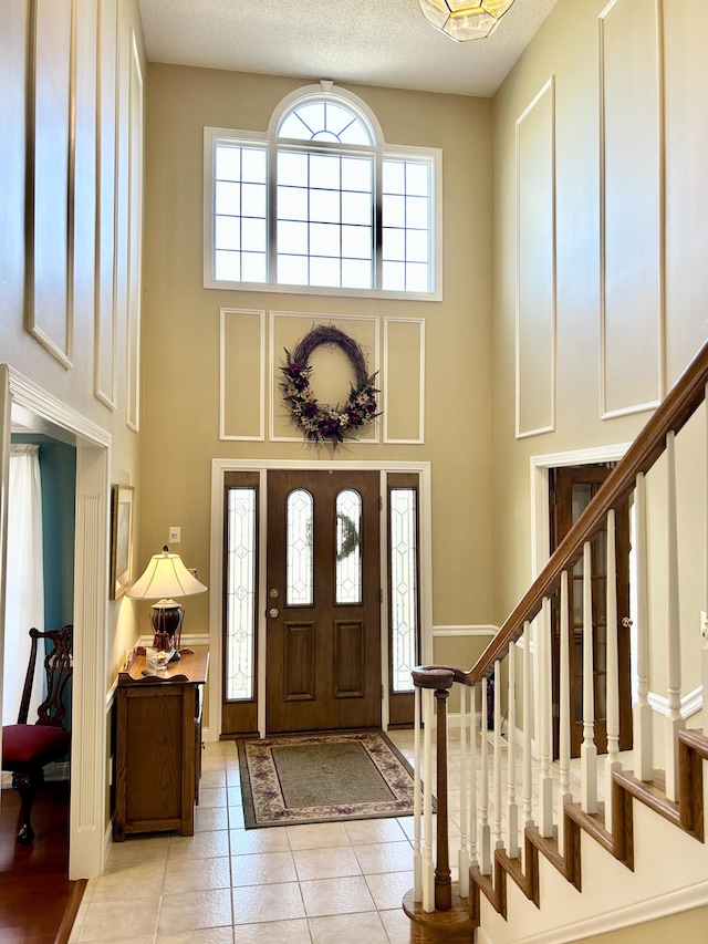 foyer featuring light tile patterned floors, a towering ceiling, stairs, and baseboards