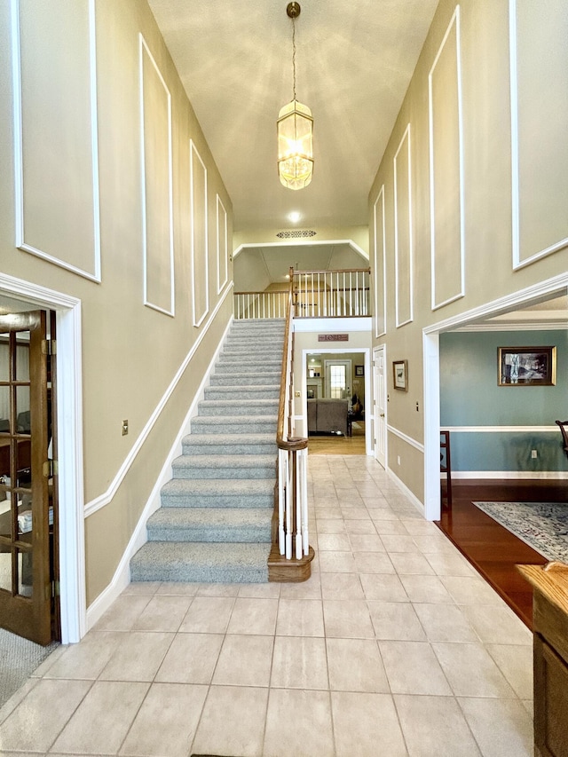 staircase featuring a towering ceiling, a chandelier, tile patterned floors, and baseboards