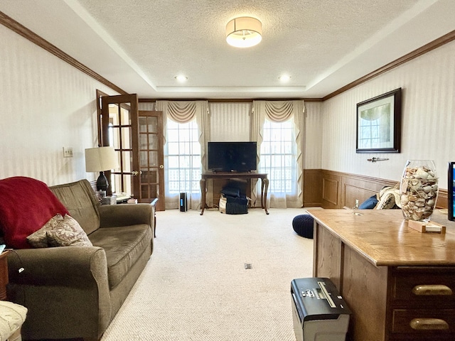 carpeted living area with a textured ceiling, a raised ceiling, a wainscoted wall, and ornamental molding