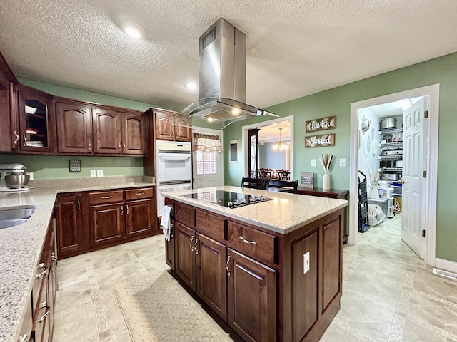 kitchen featuring glass insert cabinets, white double oven, island range hood, a center island, and black electric cooktop