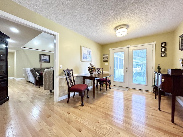 dining area with baseboards, light wood-type flooring, a textured ceiling, and french doors