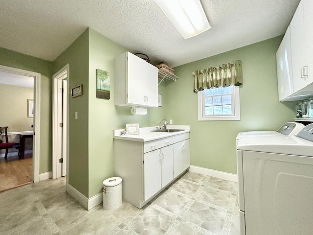 clothes washing area with cabinet space, a sink, baseboards, washing machine and dryer, and a textured ceiling