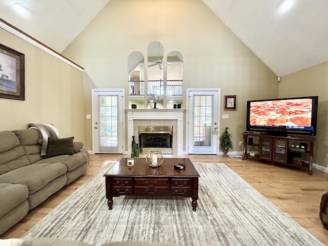 living area with a tile fireplace, high vaulted ceiling, a ceiling fan, baseboards, and wood finished floors