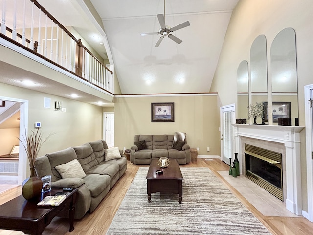 living room featuring light wood-style floors, a tiled fireplace, a ceiling fan, and high vaulted ceiling