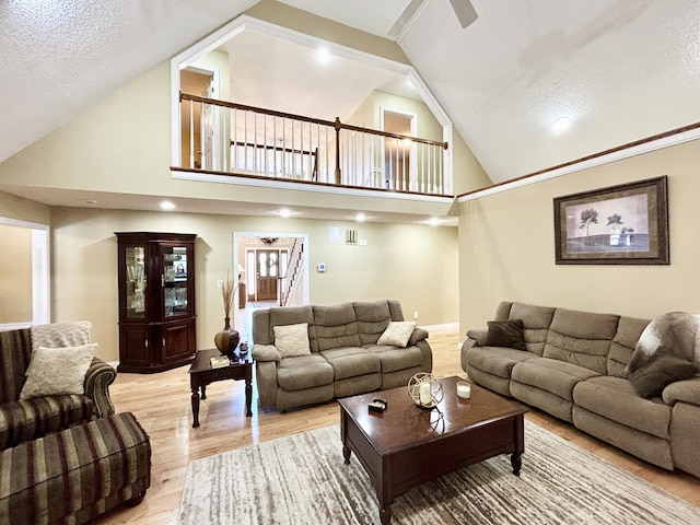 living area featuring a textured ceiling, ceiling fan, light wood-type flooring, and high vaulted ceiling