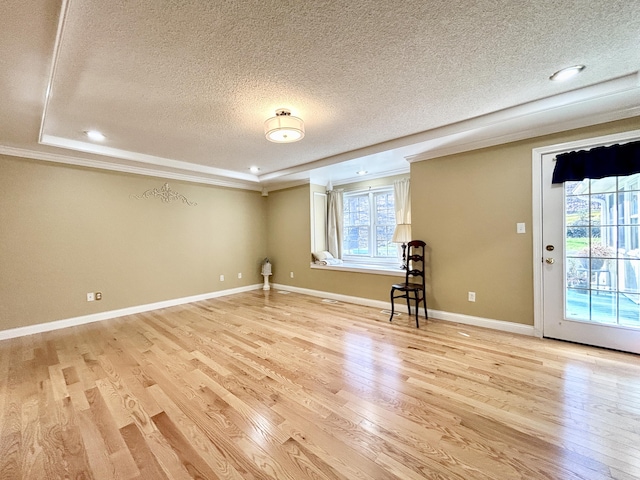 interior space with light wood-style flooring, ornamental molding, baseboards, a textured ceiling, and a tray ceiling