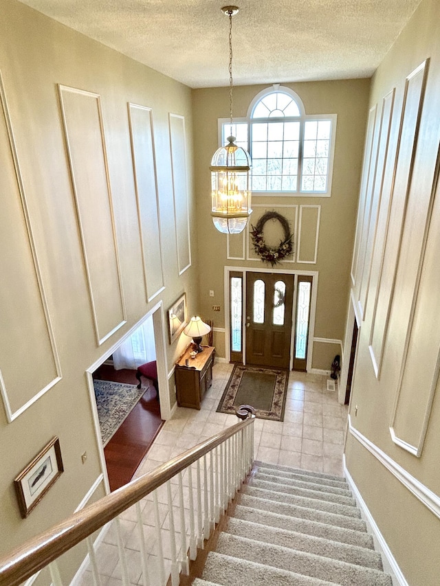 foyer featuring stairway, a textured ceiling, a notable chandelier, and tile patterned flooring