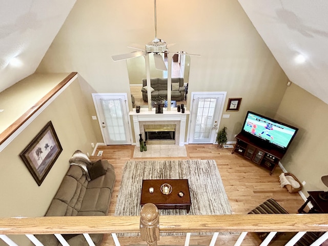living area featuring wood finished floors, a fireplace, baseboards, high vaulted ceiling, and a ceiling fan