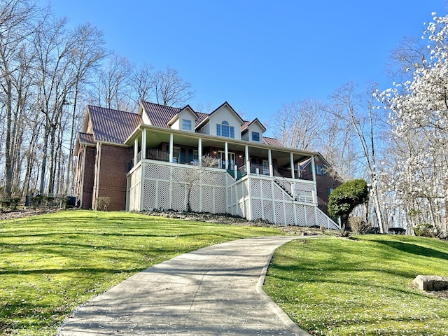 new england style home featuring a porch, brick siding, stairway, metal roof, and a front lawn