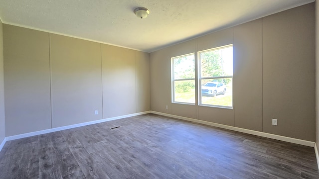 unfurnished room with dark wood finished floors, baseboards, and a decorative wall