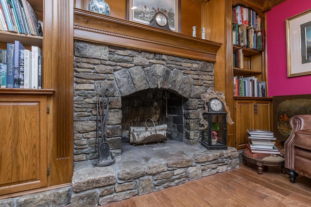 room details with built in shelves, a stone fireplace, and wood finished floors