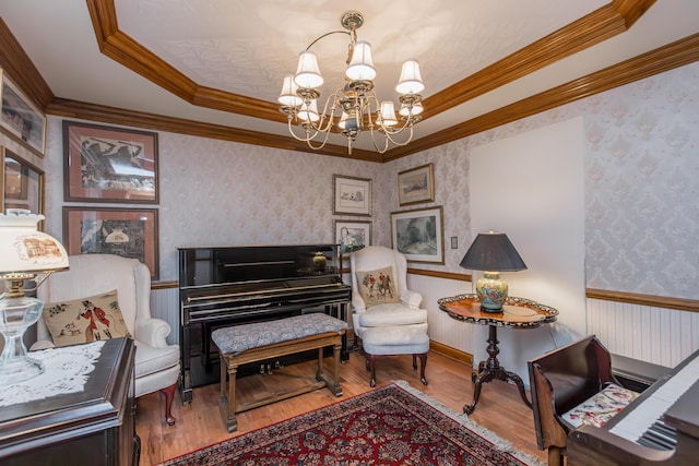 living area featuring wood finished floors, a wainscoted wall, a chandelier, ornamental molding, and wallpapered walls