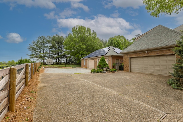 view of front of home with driveway, solar panels, brick siding, fence, and an attached garage