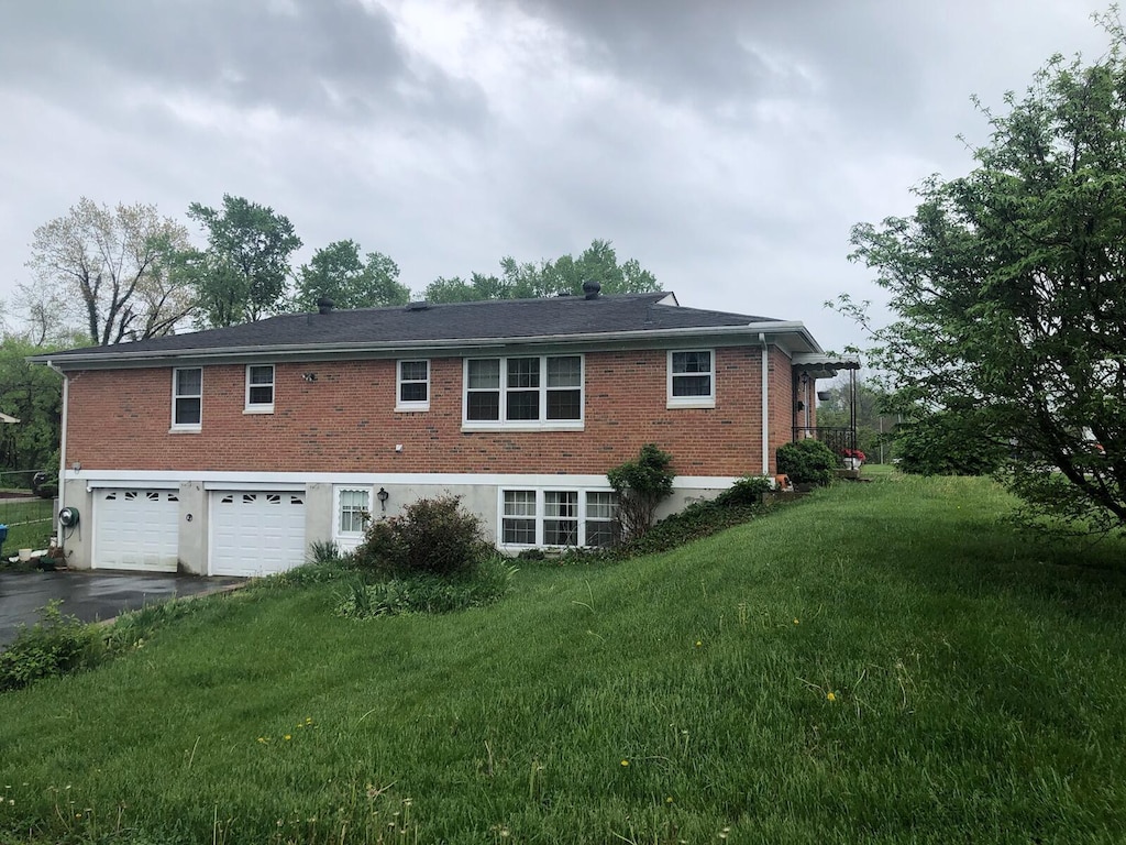 rear view of property with driveway, a yard, brick siding, and a garage