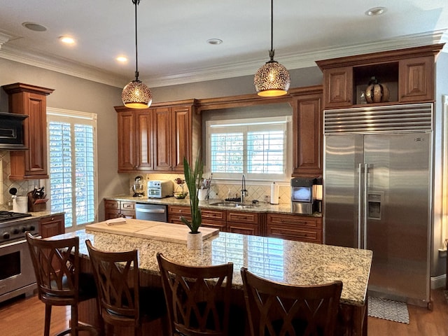 kitchen featuring a sink, tasteful backsplash, hanging light fixtures, appliances with stainless steel finishes, and wood finished floors