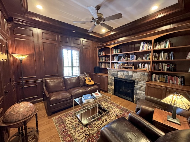 sitting room with crown molding, a ceiling fan, a stone fireplace, and light wood-style flooring