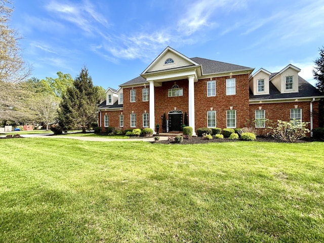 neoclassical home featuring a front yard, a shingled roof, and brick siding