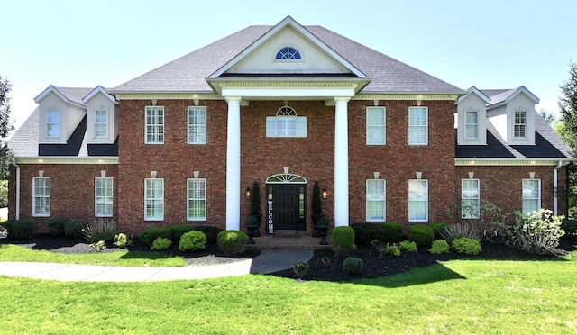 neoclassical / greek revival house featuring a front yard and brick siding